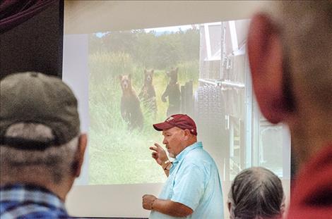 Confederated Salish and Kootenai Tribes Wildlife Biologist Stacy Courville speaks at a meeting in Arlee on Aug. 28 about the conflicts that arise as bears share land with humans on the CSKT Reservation. He points towards a photo of three bears  checking out a trap used to relocate bears. 