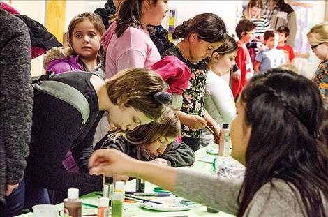 Akasha Amaya, 10, paints on raw hide along with many other children at the table.