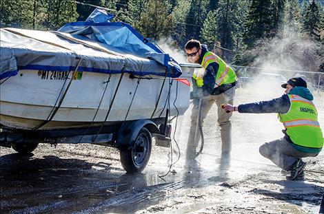 As a precautionary measure, inspectors wash a boat during the 2018 boating season that was brought to Montana from a state with a known mussel infestation. The inspector on the right holds a temperature guage to make sure the water temperature is hot enough to kill any potential mussels or larvae.