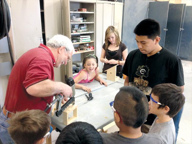 Ronan High School shop teacher Dave Edington does some drill work while his students help Sheila Hoback’s first graders make bird feeders last week.