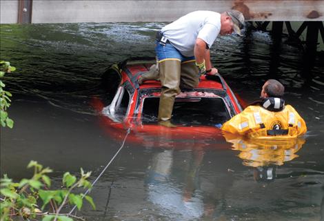 Ronan Volunteer Fire Department Sgt. Chris Atkinson and Assistant Fire Chief Dave Marmon wait for a wrecker to pull a car from the canal at Terrace Lake Road last Thursday.