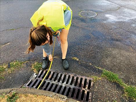 A volunteer takes a measurement of a storm drain.