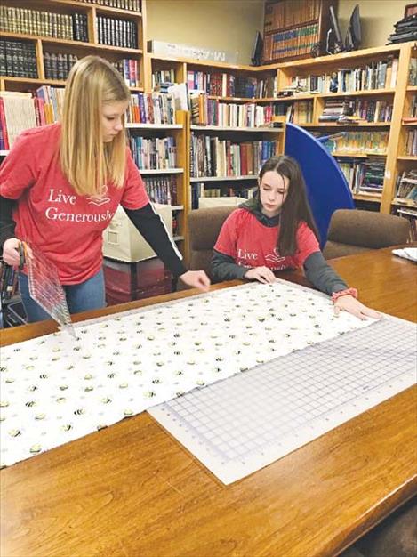Kaitlyn Stutzman and Ryleigh Bell lay out the baby blanket material for cutting.