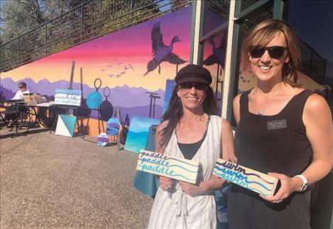 Artist Jess Bouchee and Flathead Lakers Executive Director Kate Sheridan display hand-painted signs by Bouchee that capture the spirit of summer on the lake. 