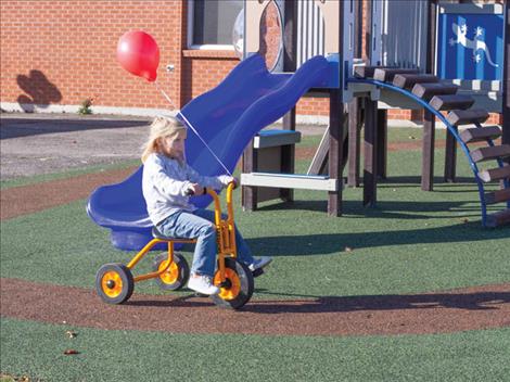 Winnie Hanson takes her red balloon for a tricycle ride along a path in the new playground.
