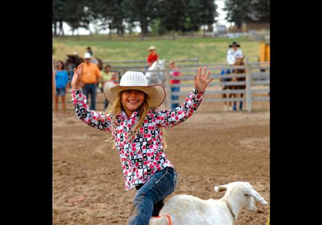 Ruby Ray grins as she signals time after tying her goat tail. From East Glacier, Ruby competes in the 7-and-under age group.