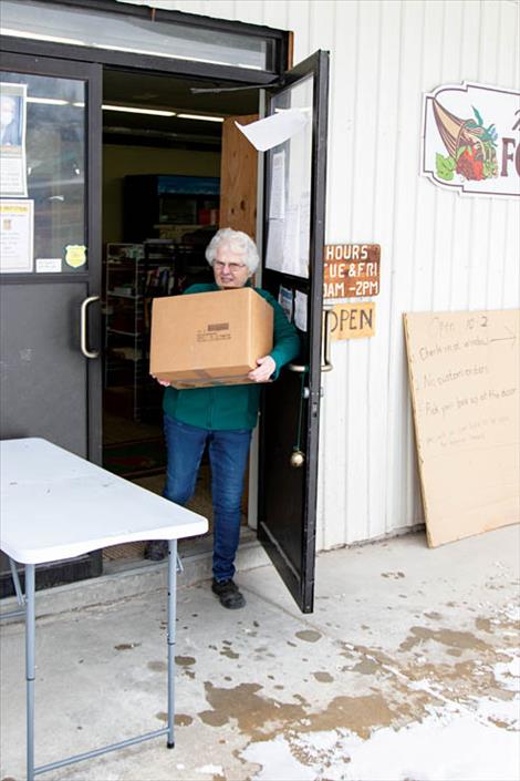 Volunteer Barbara Plouffe brings a box of food to an outside table for pick up.