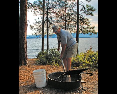 With the tools of his trade, a shovel and a bucket, Dave Gray cleans a firepit so the campsite will be ready for the next folks who come to enjoy the park.