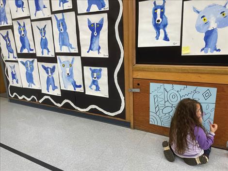  Farrah Banna helps fill in a coloring page next to a wall filled with blue dogs painted by students.