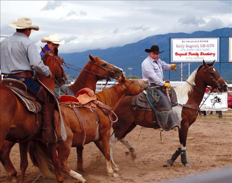 Pete White, center, unfastens the flank cinch on a saddle bronc as Bodge Whitworth dallies up and starts to drag the horse. 