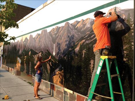 Artist Rob Gunderson, right, and his sister, Sara Gunderson, install a mural Rob painted. The mountain and forest scene is part of a continuing effort to make downtown Polson more visually appealing. 