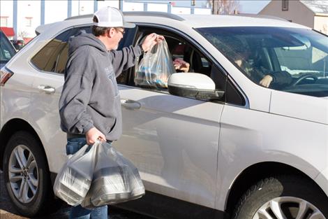 A volunteer for the Polson Community Thanksgiving Dinner hands Thanksgiving meals to a woman waiting for them.